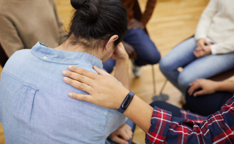 Back view of young man crying in support group with psychologist comforting him, copy space